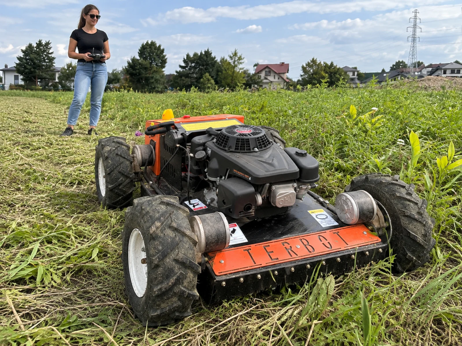 Kobieta sterująca kosiarką zdalnie sterowaną TERBOT M55 Mini podczas koszenia ogrodu